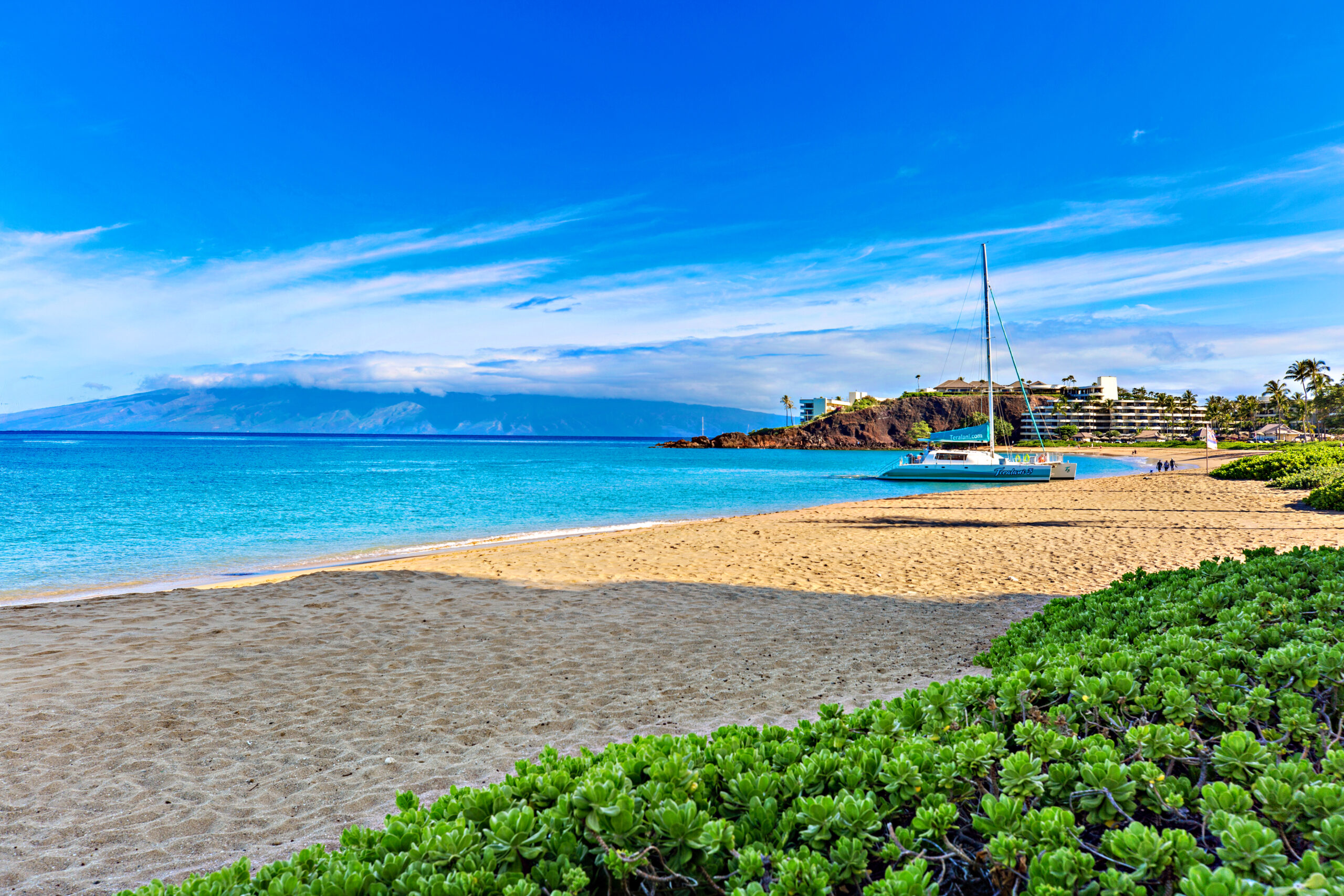 Sandy beach with clear blue water and sailboat.