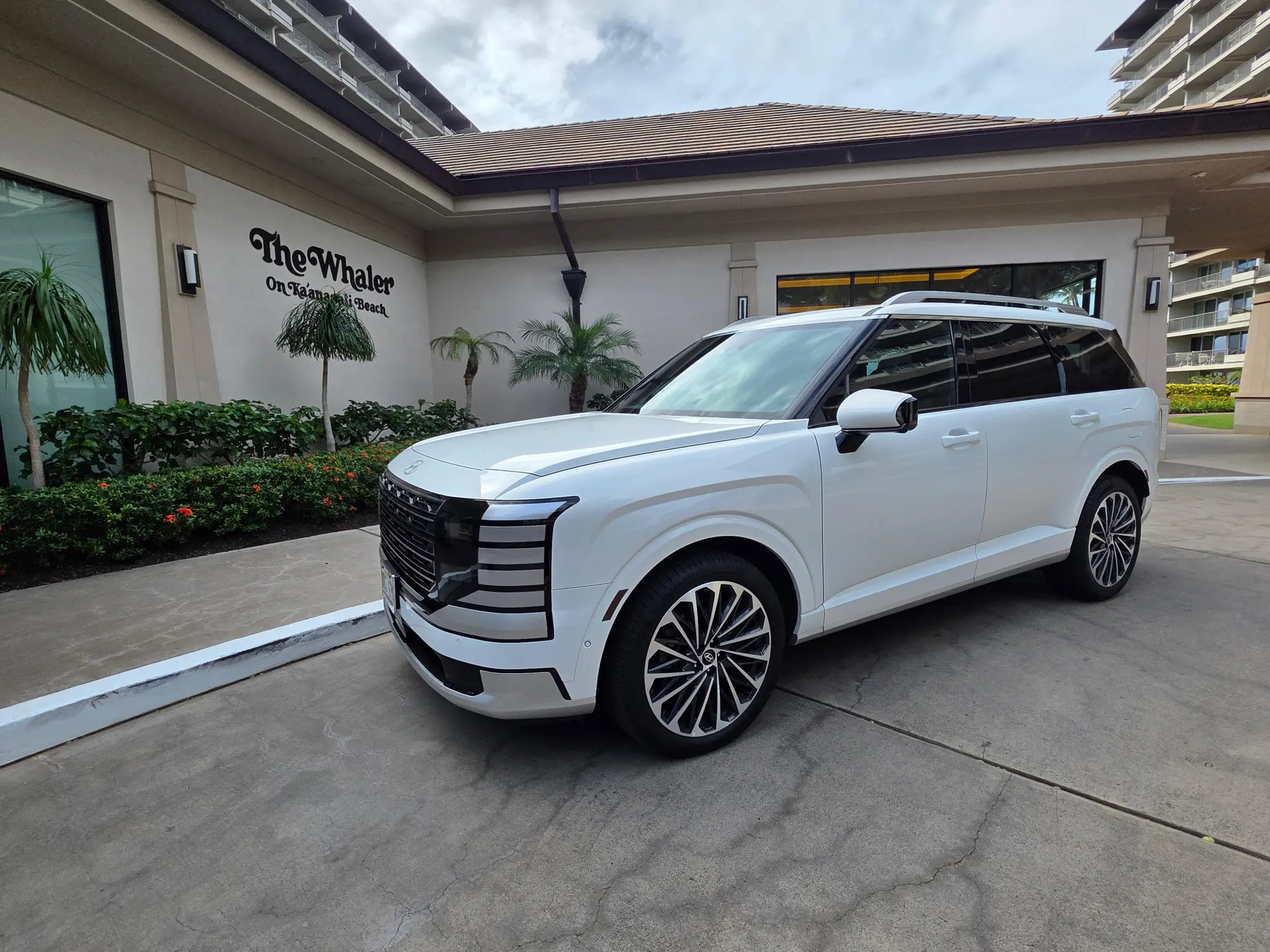 A white luxury SUV is parked at The Whaler on Kaanapali Beach, a popular spot for group rentals Kaanapali, surrounded by palm trees and greenery.