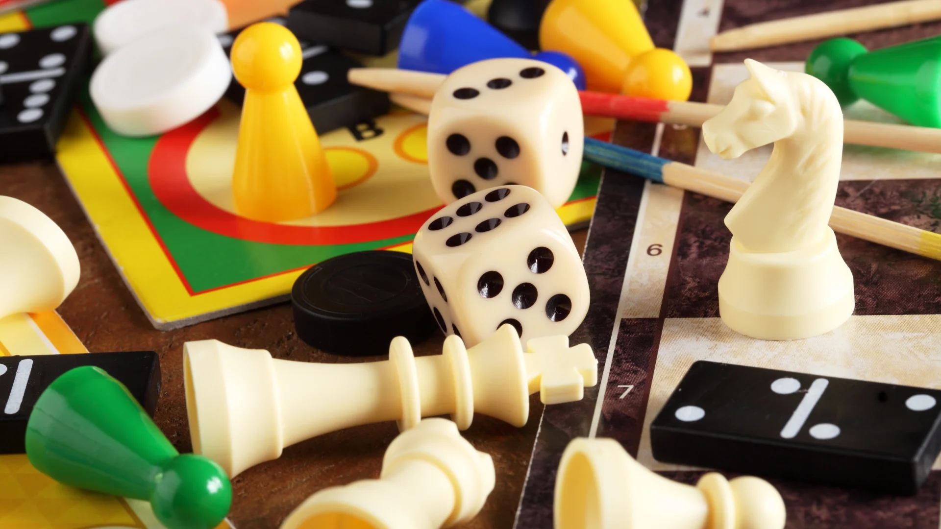 A close-up of assorted board game pieces, including dice, chess pieces, dominoes, pawns, and game boards, scattered together.