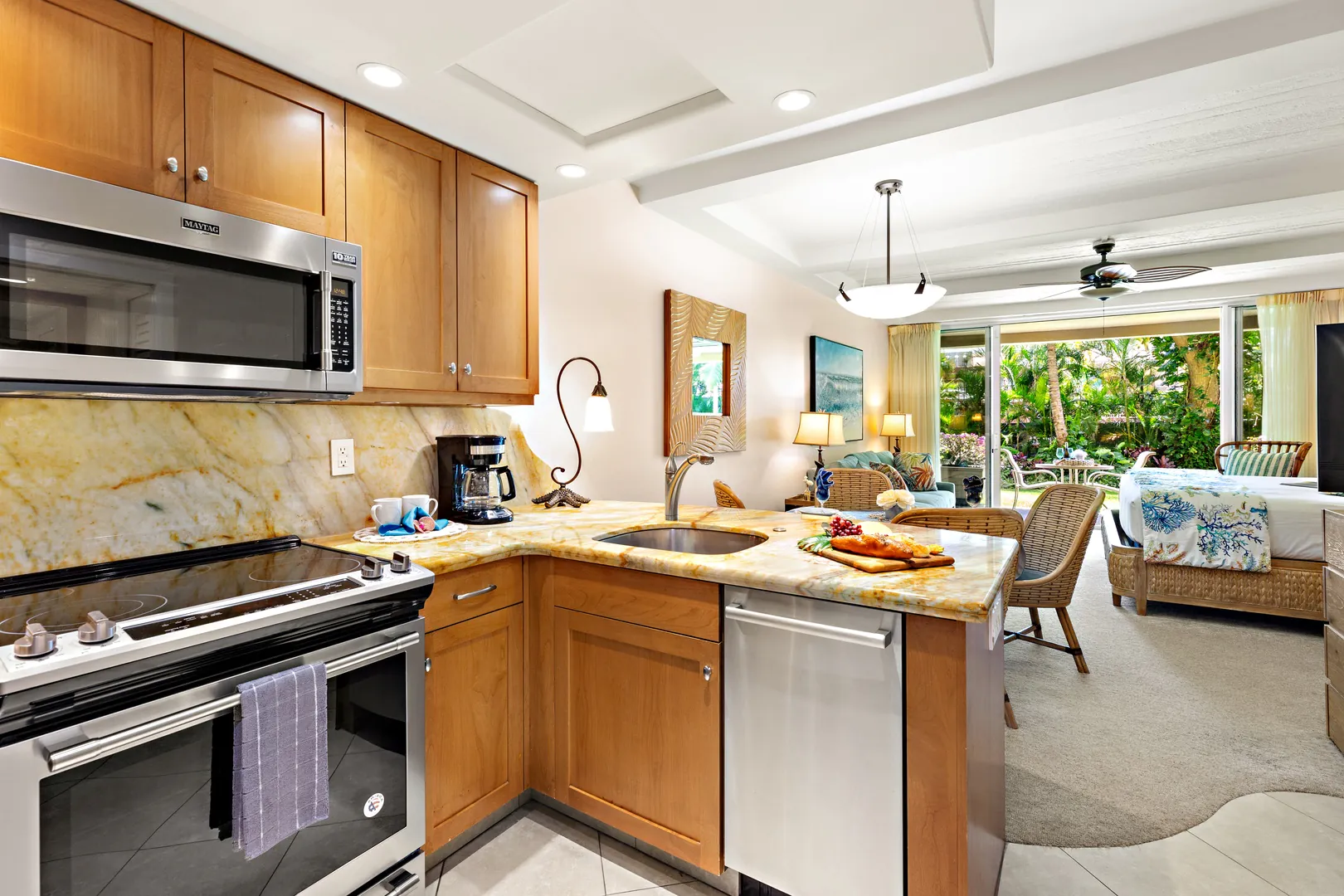 Modern kitchen with wood cabinets, marble counters, and stainless appliances opens to a bright living area near Kaanapali HI beachfront resorts.
